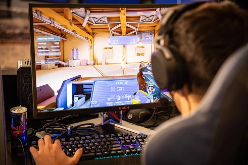 Persoon die met een headset een first-person shooter speelt op een desktopcomputer met toetsenbord en monitor.